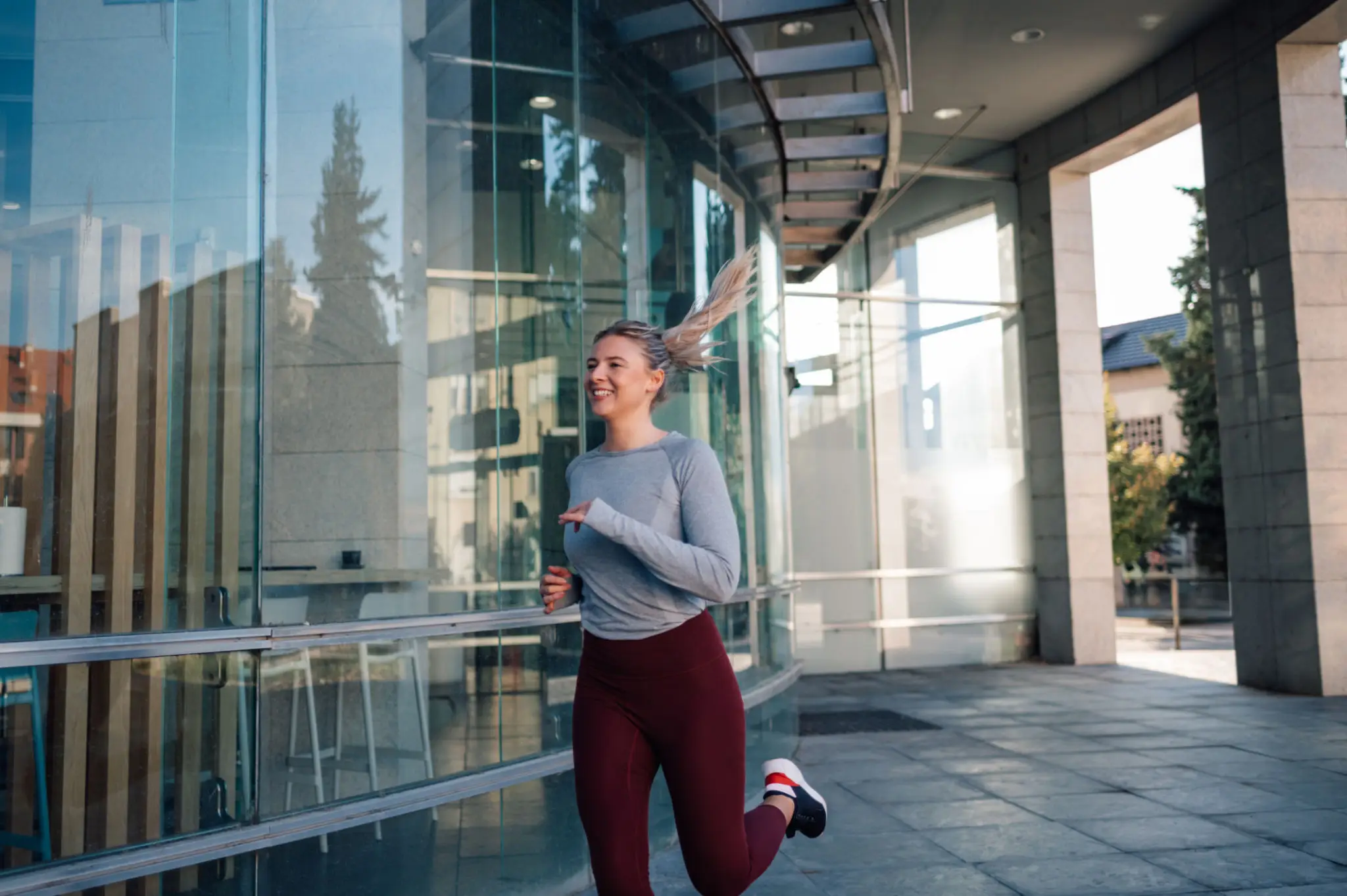 Smiling woman jogging past glass building