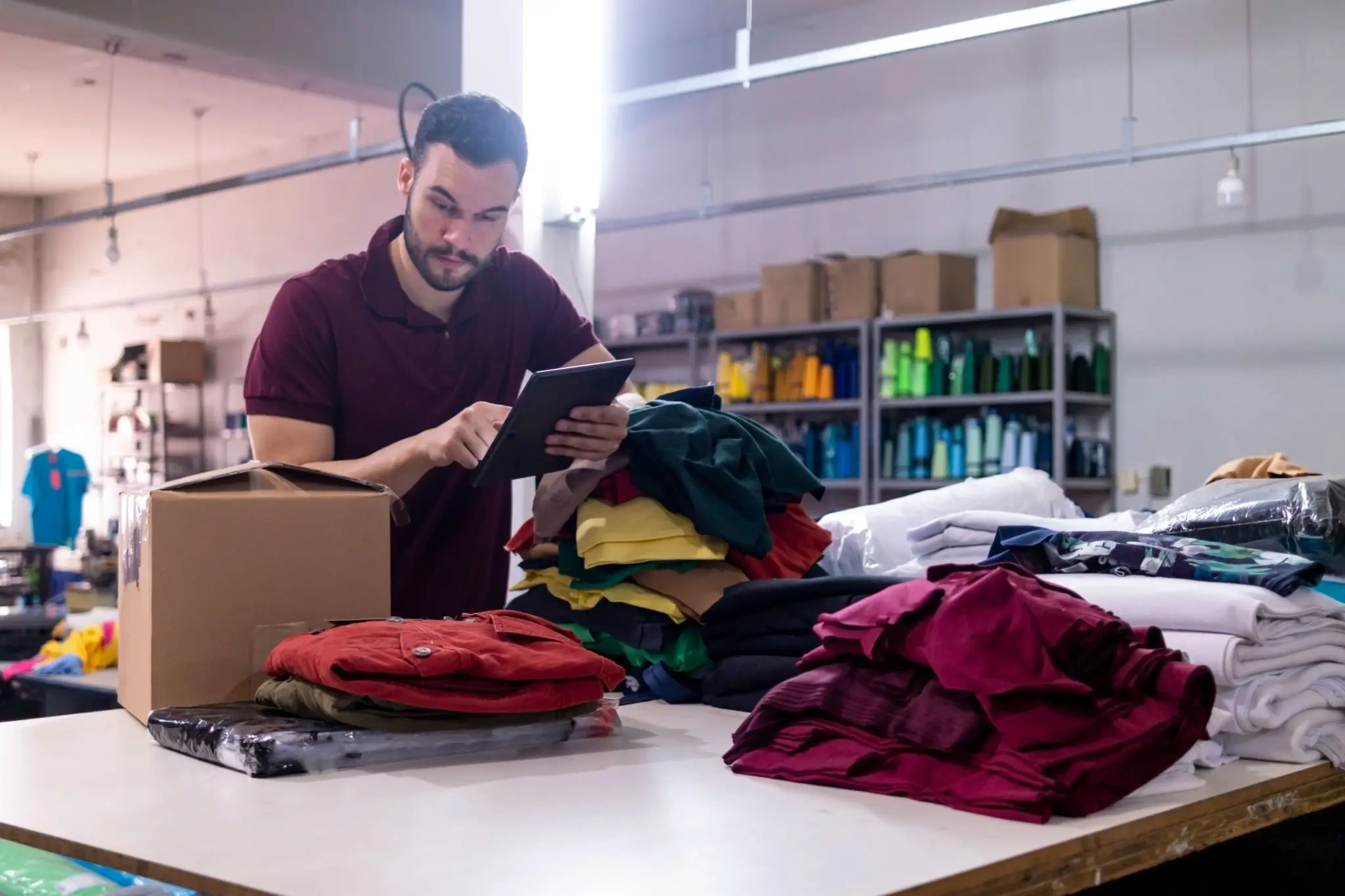 Worker checking tablet beside folded clothing